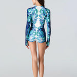 Woman wearing a blue and green patterned swimsuit on a light gray background