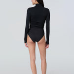 Back view of a woman wearing a black long-sleeve turtle neck rash-guard and bikini bottom.