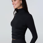 3/4 view of a woman wearing a black long-sleeve turtle neck rash-guard and bikini bottom.