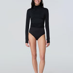 Full body view of a woman wearing a black long-sleeve turtle neck rash-guard and bikini bottom.