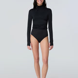Full body view of a woman wearing a black long-sleeve turtle neck rash-guard and bikini bottom.
