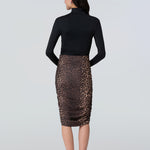 Back view of a woman wearing a black turtelneck adn leopard print midi skirt with side ruching.