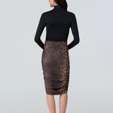 Back view of a woman wearing a black turtelneck adn leopard print midi skirt with side ruching.