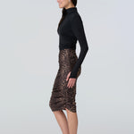Side view of a woman wearing a black turtelneck adn leopard print midi skirt with side ruching.