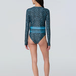 A woman wearing a long-sleeve top in a blue dot print with stripe at hem and matching bikini bottom.