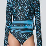 A woman wearing a long-sleeve top in a blue dot print with stripe at hem and matching bikini bottom.