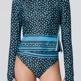 A woman wearing a long-sleeve top in a blue dot print with stripe at hem and matching bikini bottom.