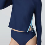 Woman wearing a navy blue long-sleeve top with a light blue side zipper and navy blue bikini bottom.