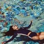 Woman wearing a blue and white colorblocked long sleeve tee and bikini bottom swimsuit in a pool