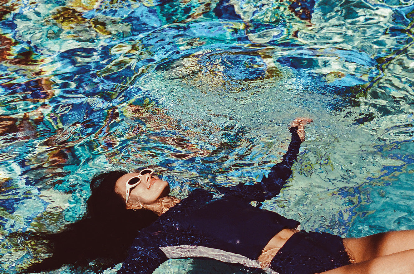 Woman wearing a blue and white colorblocked long sleeve tee and bikini bottom swimsuit in a pool