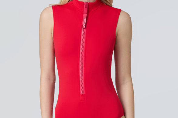 Front view of a woman in a side profile wearing a red sleeveless one-piece swimsuit and black sunglasses.
