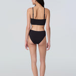 Back view of a woman wearing a black swim and sun protective bralette and bikini bottom.
