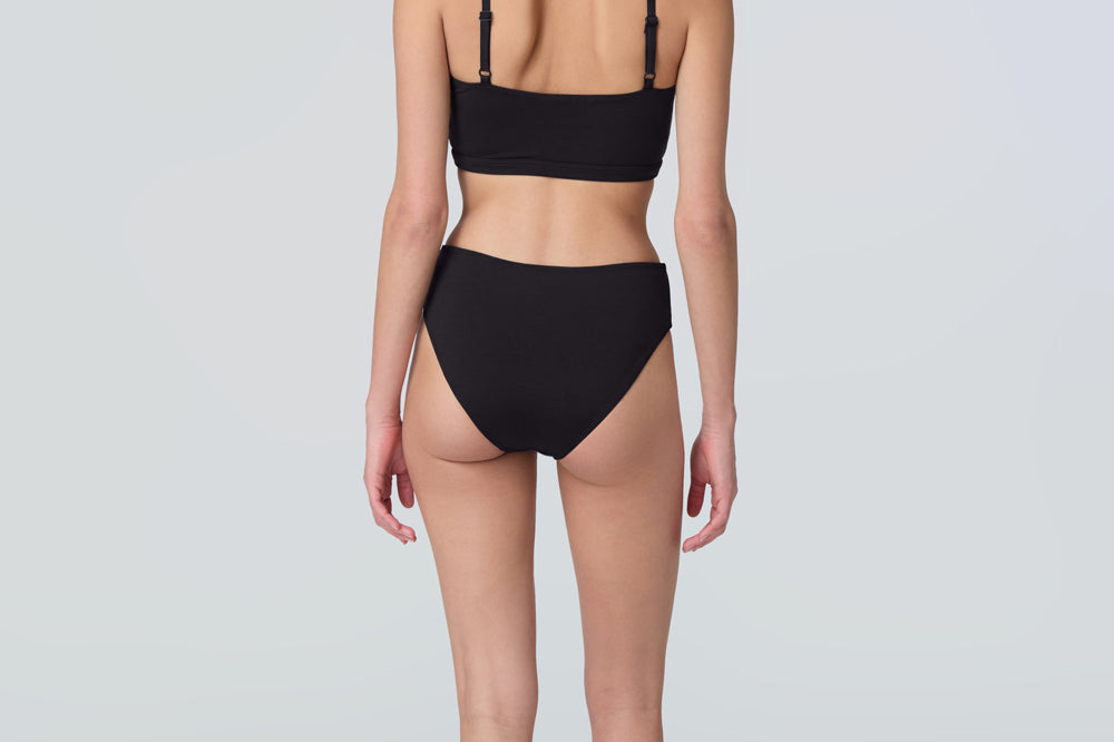 Back view of a woman wearing a black swim and sun protective bralette and bikini bottom.
