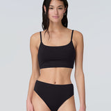 Front view of a woman wearing a black swim and sun protective bralette and bikini bottom.