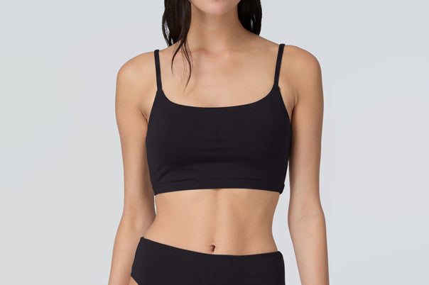 Front view of a woman wearing a black swim and sun protective bralette and bikini bottom.
