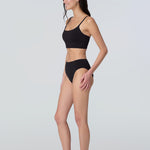 Side view of a woman wearing a black swim and sun protective bralette and bikini bottom.