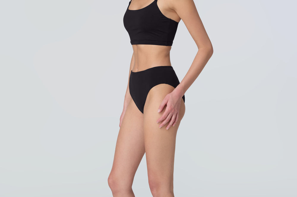 Side view of a woman wearing a black swim and sun protective bralette and bikini bottom.
