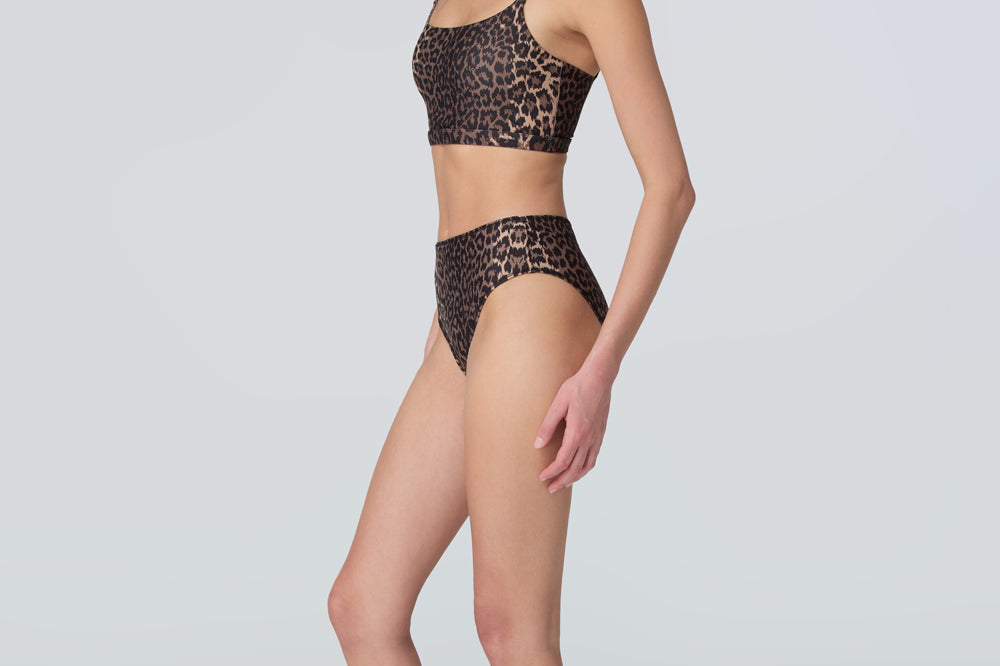 Side view of a woman wearing a leopard print swim and sun protective bralette and bikini bottom.