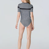 Back of a woman wearing a black and white checkered swimsuit on a light gray background
