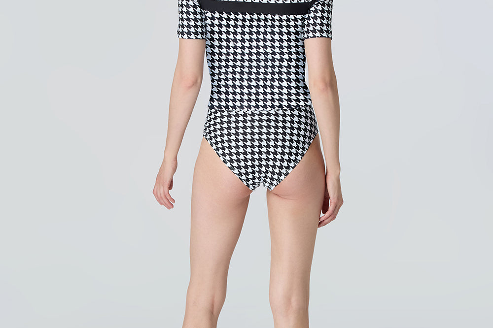 Back of a woman wearing a black and white checkered swimsuit on a light gray background