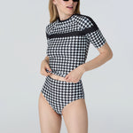 Woman wearing a black and white checkered swimsuit on a light gray background