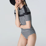 Woman wearing a black and white checkered swimsuit with a matching hat on a gray background