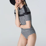 Woman wearing a black and white checkered swimsuit with a matching hat on a gray background