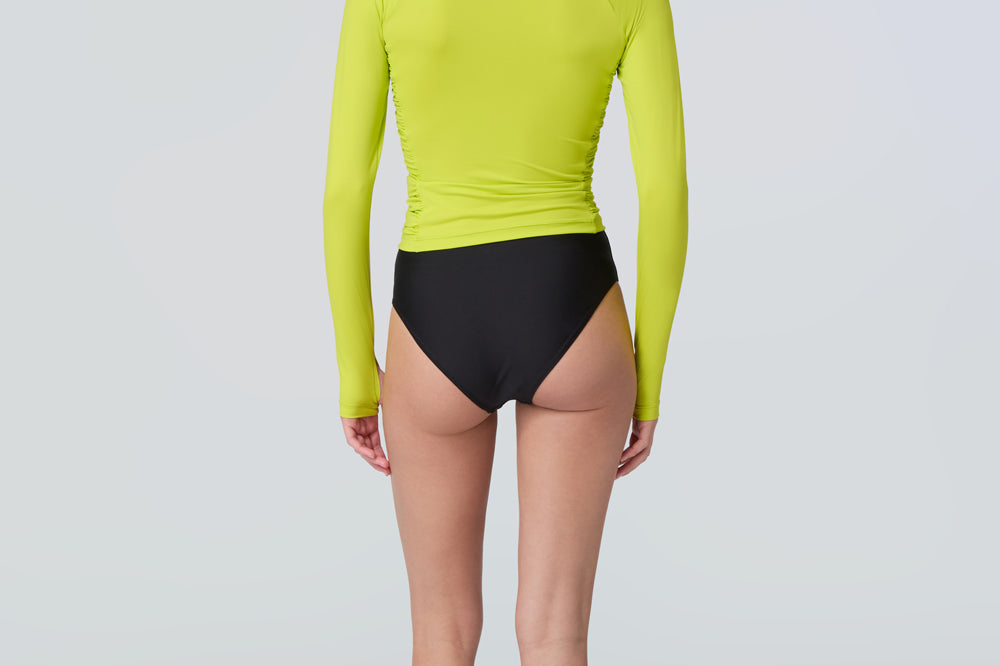 Back view of a woman wearing a lime green long-sleeve 1/2 zip rashguard with side ruching