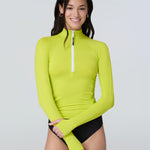 Front view of a woman wearing a lime green long-sleeve 1/2 zip rashguard with side ruching