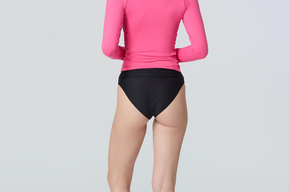 Back view of a woman wearing a pink long-sleeve rashguard with side ruching