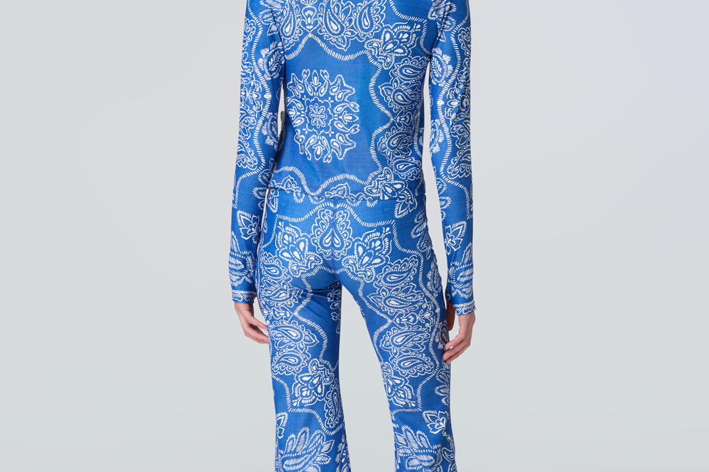 A woman wearing a long sleeve top and flare pants in a blue and white bandana print.