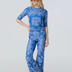 A woman wearing a short sleeve top and flare pants in a blue and white bandana print.
