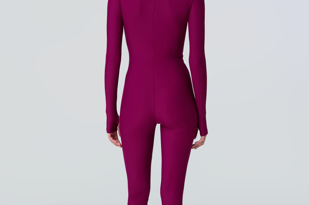 Back view of a woman wearing a long sleeve full length catsuit in dark berry with pink front zipper.