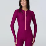 Woman wearing a long sleeve full length catsuit in dark berry with pink front zipper.