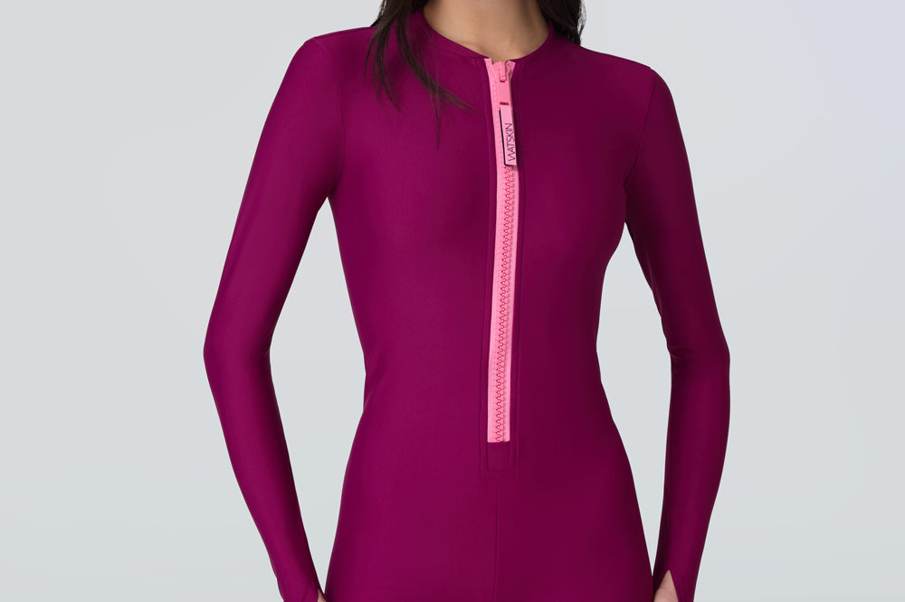 Woman wearing a long sleeve full length catsuit in dark berry with pink front zipper.