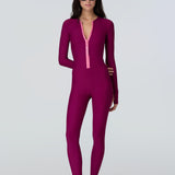 front view of a woman wearing a long sleeve full length catsuit in dark berry with pink front zipper.