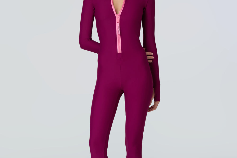 front view of a woman wearing a long sleeve full length catsuit in dark berry with pink front zipper.