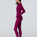 Side view of a woman wearing a long sleeve full length catsuit in dark berry with pink front zipper.