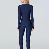 Back view of a woman wearing a navy blue long-sleeve full-body catsuit swimsuit with a light blue front zipper.