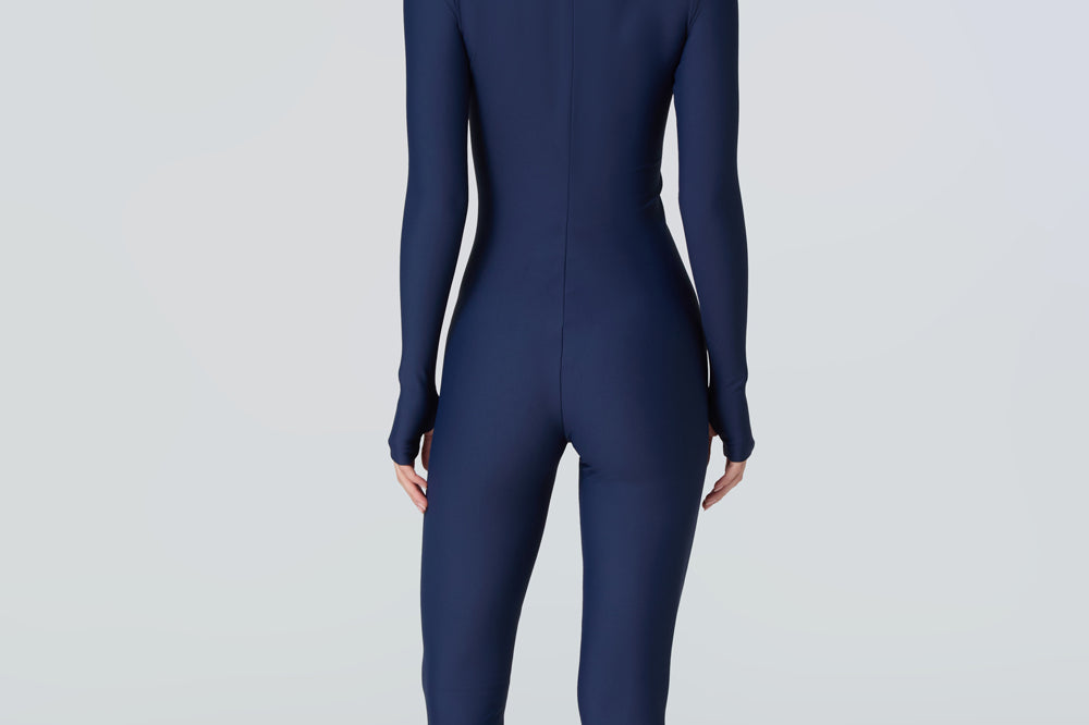 Back view of a woman wearing a navy blue long-sleeve full-body catsuit swimsuit with a light blue front zipper.