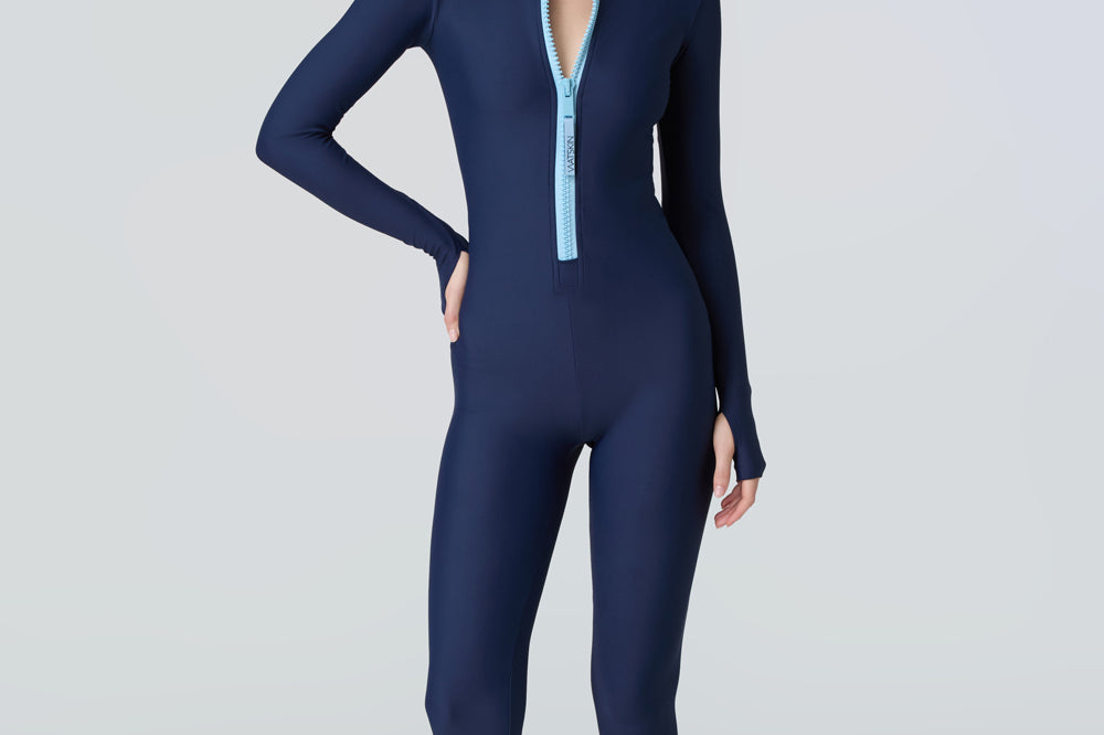 Front view of a woman wearing a navy blue long-sleeve full-body catsuit swimsuit with a light blue front zipper.