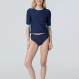 Front view of a woman wearing a navy blue short-sleeve top with light blue cuffs and neck trim and navy bikini bottom.