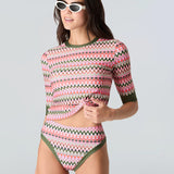 Close up front view of a woman wearing a pink and green wavy striped patterned short sleeve swim top with green sleeve cuff and bikini bottom with green trim on a white background