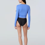 Back view of a woman wearing a light blue long-sleeve sun protective tee and black bikini bottom