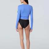 Back view of a woman wearing a light blue long-sleeve sun protective tee and black bikini bottom