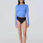 Front view of a woman wearing a light blue long-sleeve sun protective tee with side ruching and arm zip pocket and black bikini bottom