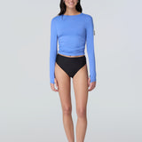 Front view of a woman wearing a light blue long-sleeve sun protective tee with side ruching and arm zip pocket and black bikini bottom