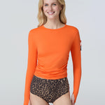 Front view of a woman wearing an orange long-sleeve sun protective tee with side ruching and arm zip pocket and leopard print bikini bottom