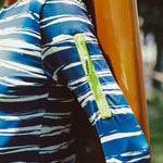 Close-up of a person wearing a blue and white striped shirt with a yellow zipper pocket on the arm in a tropical outdoor setting