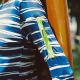Close-up of a person wearing a blue and white striped shirt with a yellow zipper pocket on the arm in a tropical outdoor setting